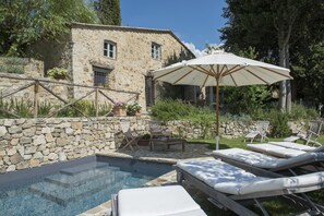 Un bâtiment en pierre avec une piscine, des chaises longues et un parasol.
