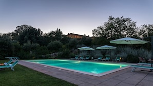 A rectangular swimming pool with lounge chairs and umbrellas, surrounded by greenery and a building in the background. - Villa Il Foramasso 10 2 (Casole d'Elsa)