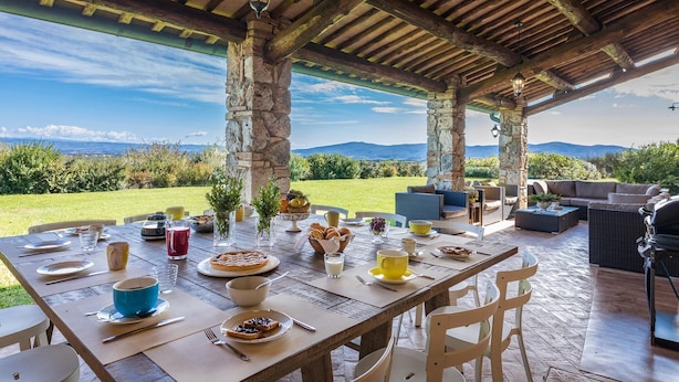 An outdoor dining area with stone pillars, a wooden table set for breakfast, and a view of the countryside. - Villa Il Foramasso 10 2 (Casole d'Elsa)