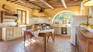 A rustic kitchen with wooden cabinets, a dining table, and a large window. - Villa Il Foramasso 10 2 (Casole d'Elsa)