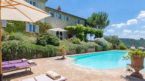 Relax by the serene pool surrounded by lush greenery and a traditional stone building.