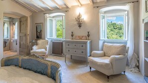 Classic design features a traditional bed, armchair, and dresser, with a view of lush greenery outside.