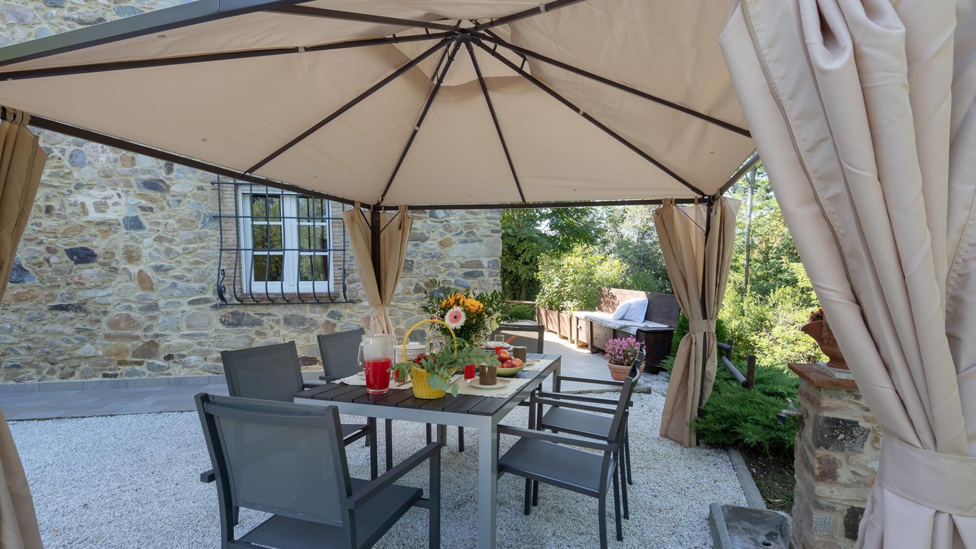 An outdoor patio with a table set for dining, surrounded by stone walls and a stone window.