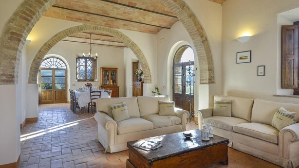 A spacious living area with a fireplace, a dining table, and a kitchen in the background. - Alborata 10 in Montalcino (Montalcino)