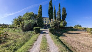 A villa with a gravel path leading to a central staircase, surrounded by neatly trimmed hedges and tall cypress trees. - Villa Palazzaccio 26 (Arezzo)
