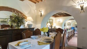 A dining area with a long table set for a meal, surrounded by chairs. There are decorative vases with flowers on the table, and a lamp is visible on the wall. - Villa Palazzaccio 26 (Arezzo)