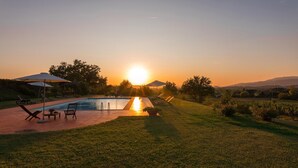 A pool area with lounge chairs and umbrellas, surrounded by grass and trees, during sunset. - Villa Palazzaccio 26 (Arezzo)