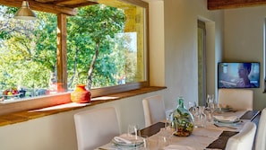 Uma sala de jantar com uma mesa posta para dois, uma janela com vista para árvores e uma televisão na parede.