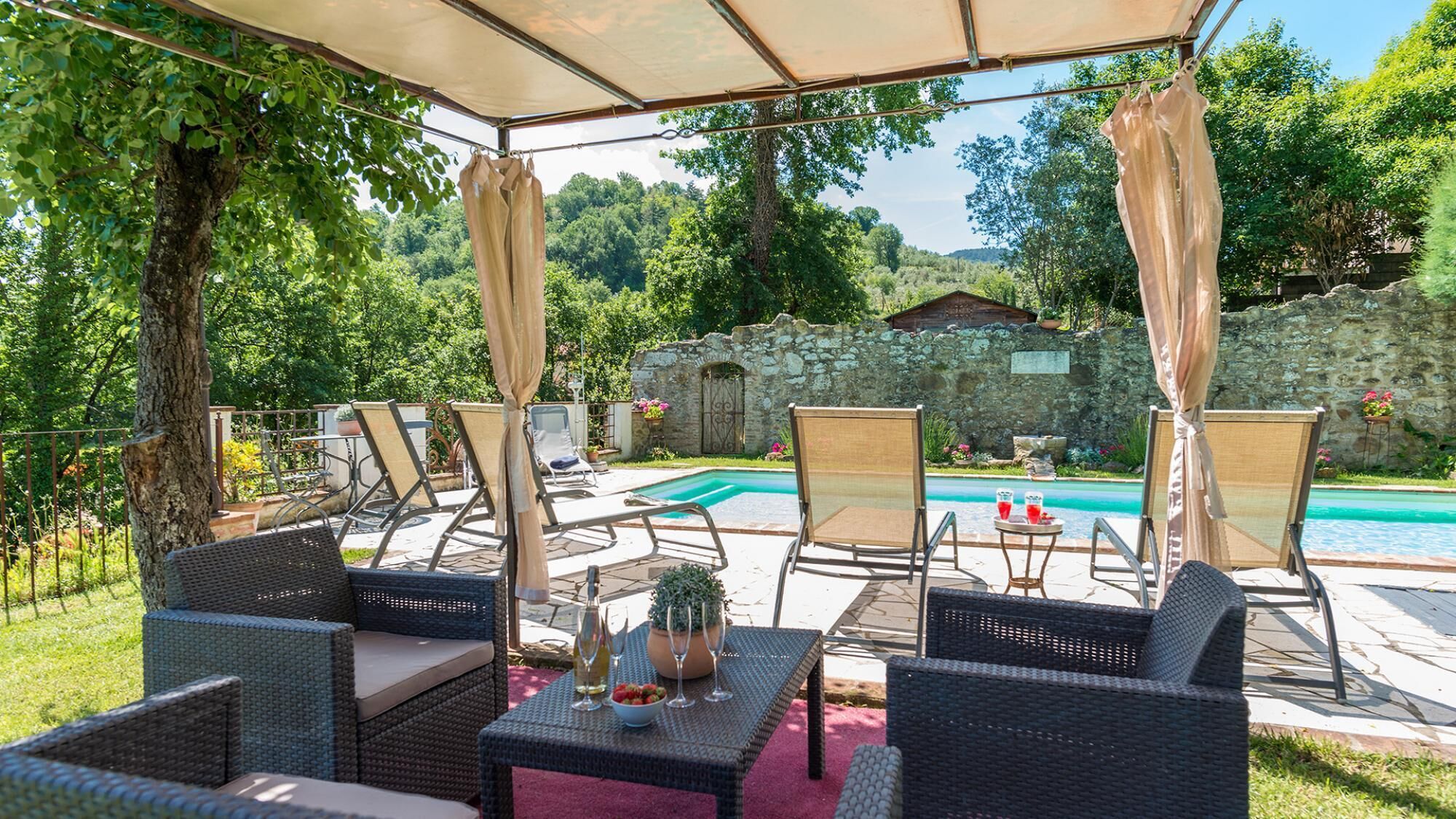 Une terrasse extérieure avec des meubles en osier, une piscine et un mur de pierre en arrière-plan.