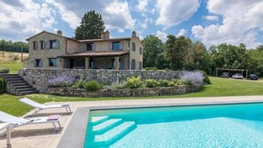 A stone house with a pool, surrounded by a garden and a clear sky. - Villa Le Fontane 12 (Todi)