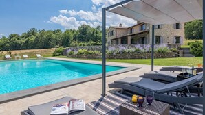 A swimming pool with lounge chairs and a table with drinks, surrounded by a stone building and greenery. - Villa Le Fontane 12 (Todi)
