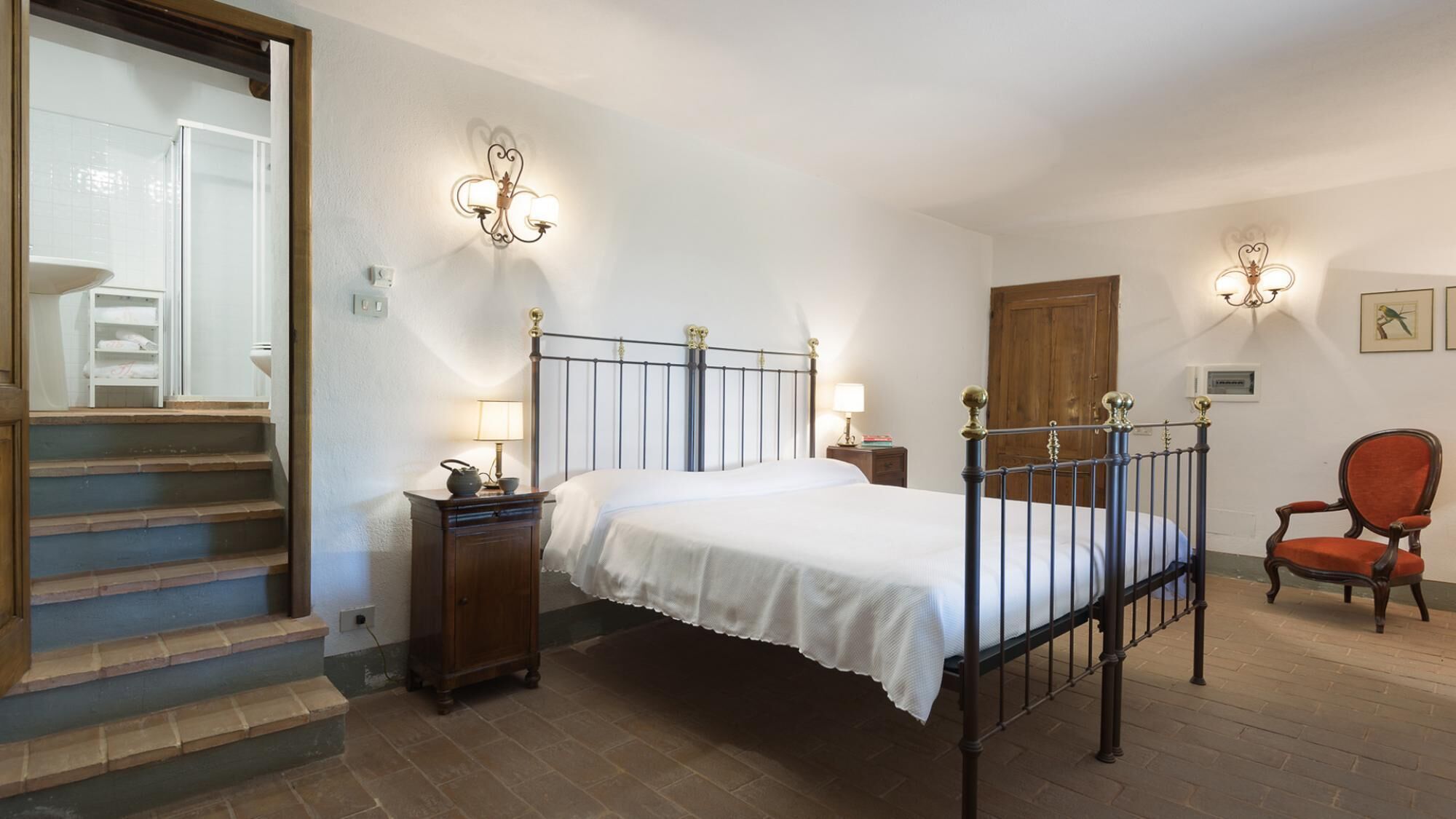 A bedroom with a bed, bedside tables, a chair, and a staircase leading to a bathroom.