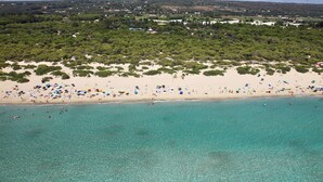 Una vista aerea di una spiaggia con acque turchesi cristalline, una riva sabbiosa e una fitta area boschiva sullo sfondo.