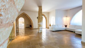 Un'ampia zona giorno con un divano bianco, pavimento in pietra e porte ad arco.