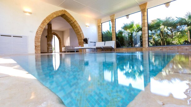 Una piscina con acqua cristallina, un arco in pietra e una zona relax con vista sulle palme.