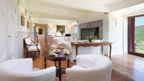 A spacious living room with a wooden floor, white furniture, and a large window offering a view of the outdoors. - Villa La Poiana 10 in Radda in Chianti (Radda in Chianti)