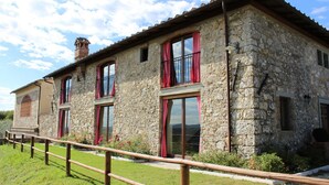 A stone building with multiple windows, a wooden fence, and a clear sky. - Villa La Poiana 10 in Radda in Chianti (Radda in Chianti)