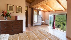 A spacious room with wooden floors, a large mirror, a dresser, and a view of a lush green landscape through a balcony. - Villa La Poiana 10 in Radda in Chianti (Radda in Chianti)