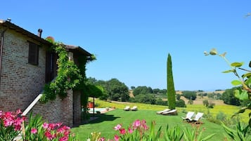 Um edifício de tijolos com um jardim, uma árvore alta e uma piscina.