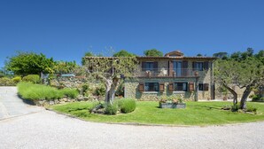A two-story stone house with a balcony, surrounded by well-maintained gardens and trees. - Antiche Pietre 10 in Tuoro sul Trasimeno (Tuoro sul Trasimeno)