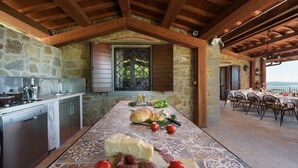 A rustic kitchen with stone walls, wooden beams, and a dining area with a table set for a meal. - Antiche Pietre 10 in Tuoro sul Trasimeno (Tuoro sul Trasimeno)