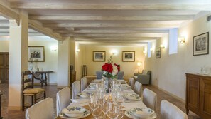 Un comedor con una mesa larga dispuesta para una comida, rodeada de sillas. Hay cuadros en las paredes, un aparador de madera y una lámpara a la derecha.