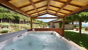 A hot tub under a wooden pergola with a stone house and greenery in the background. - Antiche Pietre 10 in Tuoro sul Trasimeno (Tuoro sul Trasimeno)