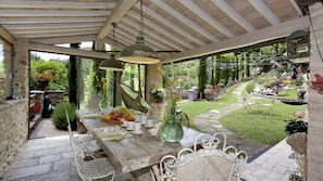 Une terrasse extérieure avec une table en bois rustique, mise pour le thé, entourée de chaises en métal blanc.