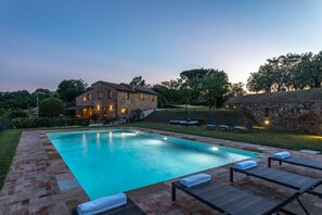 Piscina com espreguiçadeiras e um edifício de pedra ao fundo.