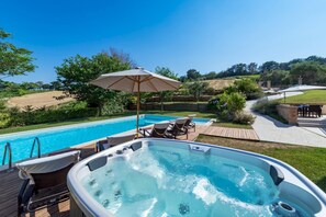 Una vasca idromassaggio con un pontile in legno, una piscina e un patio con mobili da esterno.