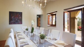 A dining room with a long table set for a meal, a chandelier, and a painting on the wall.
