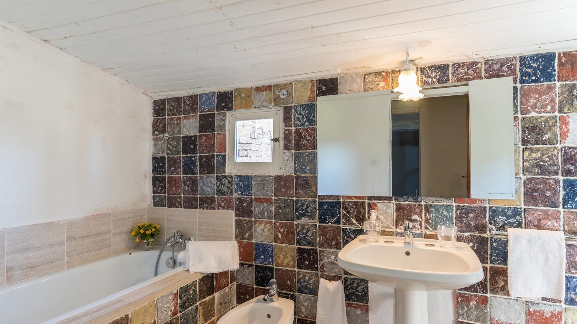 A bathroom with a tiled mosaic wall, a bathtub, a sink, and a mirror.