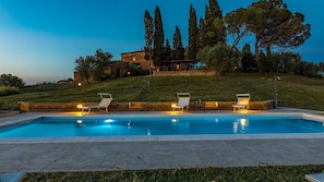 A swimming pool with three sun loungers, a stone patio, and a hillside with trees and a house in the background. - Casale Rasa 16 2 in Asciano (Asciano)