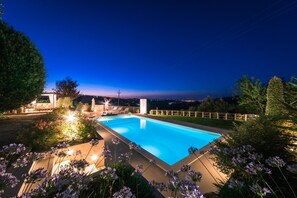 A rectangular swimming pool surrounded by a wooden deck, with a view of a cityscape at dusk.