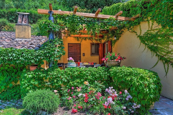 A cozy outdoor seating area with a table and chairs, surrounded by lush greenery and flowering plants.