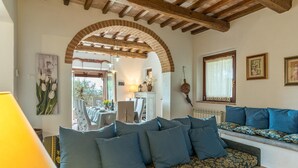A cozy living room with a sofa, a dining area with a table set for two, and a view of the outdoors through an arched doorway. - Casale Montegiovi 6 4 (Castel del Piano)
