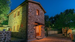 A stone building with a sloped roof and a wooden door, surrounded by a cobblestone courtyard and trees. - Casale Montegiovi 6 4 (Castel del Piano)