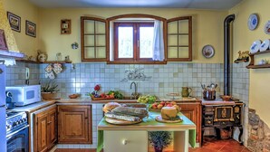 A kitchen with wooden cabinets, a tiled backsplash, a window with curtains, and various kitchen items on the counter. - Casale Le Conce 6 (Castel del Piano)