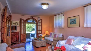 A cozy living room with a fireplace, a television, wicker furniture, and a view of the outdoors. - Casale Le Conce 6 (Castel del Piano)