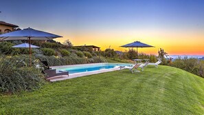 A swimming pool with lounge chairs and umbrellas, surrounded by well-maintained grass and bushes, with a view of the sunset and distant mountains. - Casale Le Conce 6 (Castel del Piano)