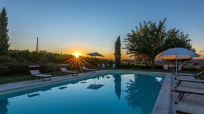 A swimming pool with lounge chairs and umbrellas, surrounded by greenery and a sunset view. - Il Fitto 10 in Cortona (Cortona)