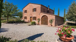 A two-story brick building with a gravel driveway, arched doorways, and a large wooden door. - Il Fitto 10 in Cortona (Cortona)