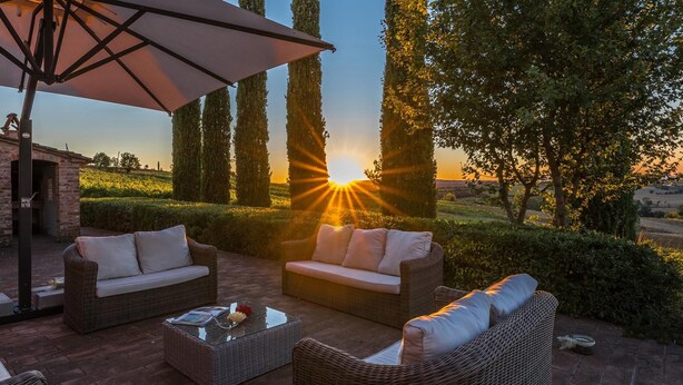 An outdoor seating area with wicker furniture and a large umbrella, overlooking a scenic landscape with trees and a sunset. - Il Fitto 10 in Cortona (Cortona)
