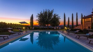 A pool with lounge chairs and umbrellas, surrounded by trees and a sunset view. - Il Fitto 10 in Cortona (Cortona)