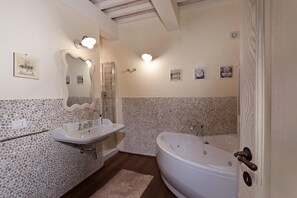 A bathroom with a stone mosaic wall, a large bathtub, a double sink, and a mirror with a wavy frame. - Casale Delle Lavande 10 (Todi)