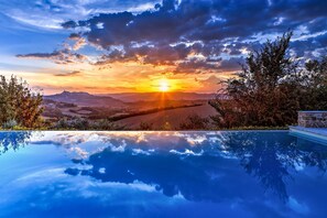 A pool reflecting a sunset over a valley with hills and a stone wall on the right. - Casale Delle Lavande 10 (Todi)