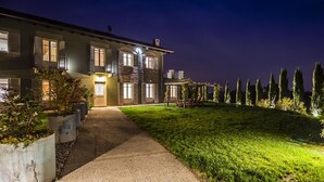 Une maison à deux étages, avec une allée pavée menant à l’entrée, entourée d’une pelouse bien entretenue et de grands arbres.