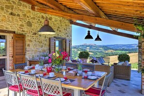 Ein rustikales Steinhaus mit einem für das Frühstück gedeckten Holztisch, umgeben von Korbmöbeln und Blick auf sanfte Hügel.