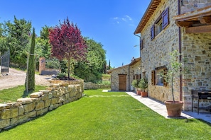 Traditional stone building with a well-maintained lawn and potted plants, surrounded by a stone wall and featuring a charming entrance.