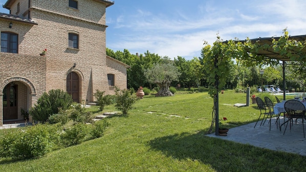 A rustic stone building with a garden, outdoor seating, and a pool area.